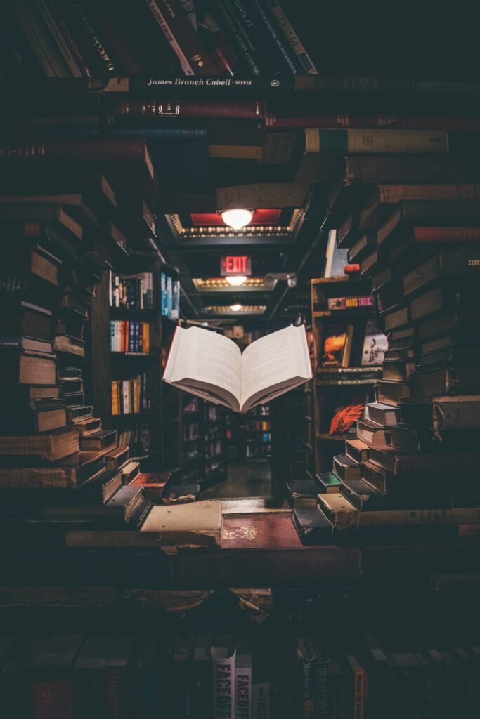 Buku terbuka melayang di antara tumpukan buku di perpustakaan